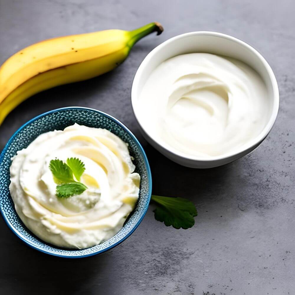 Two bowls of yoghurt and mashed banana on a kitchen bench with a whole banana